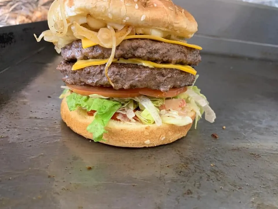 A double cheeseburger with grilled onions, lettuce and tomato on the griddle