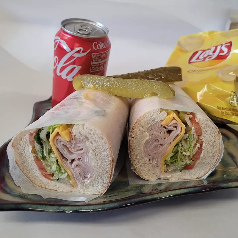 A turkey and cheese wrap with a pickle, beside a soda and a bag of chips
