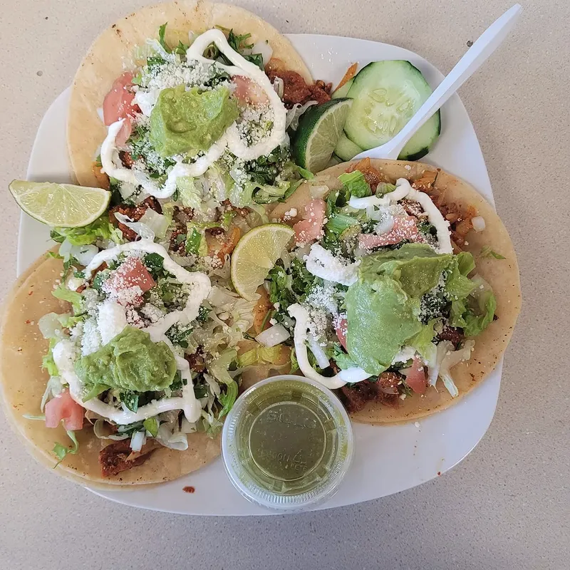 Four tacos topped with guacamole, crema and cotija