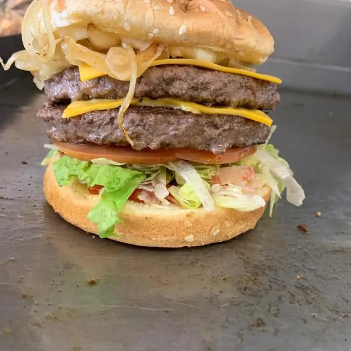 A double cheeseburger with grilled onions, lettuce and tomato on the griddle