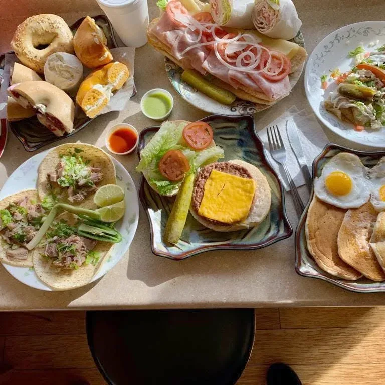 A spread of bagels, tacos, a cheeseburger, pancakes and eggs, and a cold cut platter