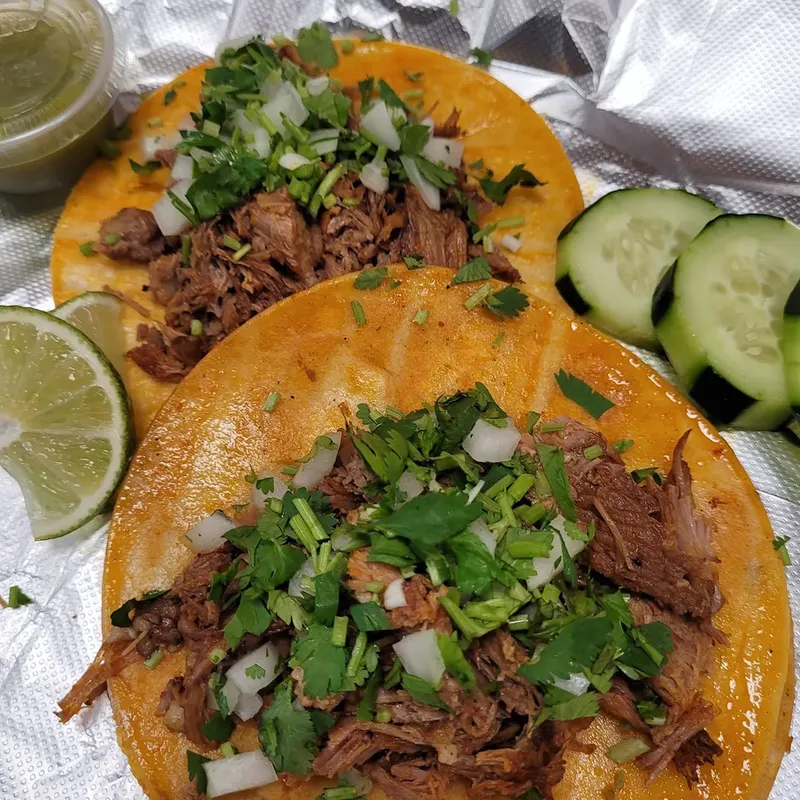 Birria-style tacos on orange tortillas with cilantro, onion and lime