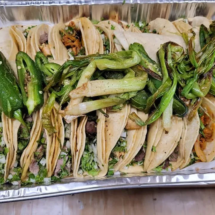 A tray of tacos with grilled scallions and jalapeños